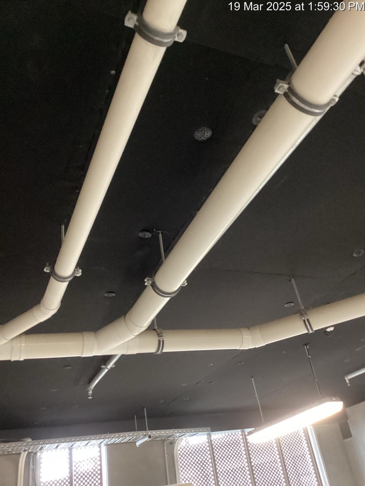 Black soffit liner installed to a carpark ceiling, cut around pipework and hangers